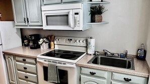Une cuisine avec des meubles blancs, un four à micro-ondes, une cuisinière et un évier.