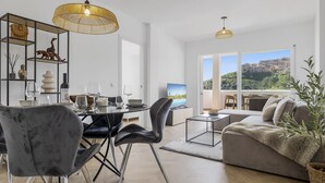 A modern living room with a dining area, a sofa, and a view of a mountainous landscape. - Rosa | Sea views - pool - terrace (Mijas Costa)
