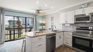 Una cocina moderna con armarios blancos, electrodomésticos de acero inoxidable, encimera de mármol y vistas al exterior.