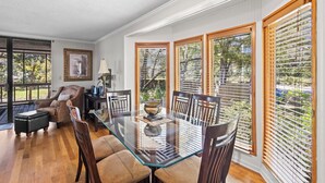 A dining area with a glass table, wooden chairs, and a view of the outdoors through large windows with blinds. - Cheyenne Retreat Pet Friendly Boater's Paradise (Orange Beach)