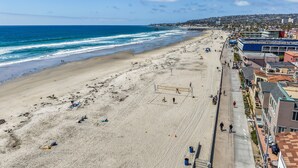A beach with a volleyball net, a pier in the background, and buildings along the shore. - Dream 2-Story Home w/Deck, A/C, Hot Tub, Gas Grill, W/D - Walk to the Beach (San Diego)