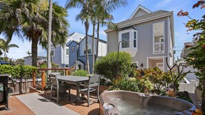 A hot tub on a wooden deck with a table and chairs, surrounded by palm trees and a house in the background. - Dream 2-Story Home w/Deck, A/C, Hot Tub, Gas Grill, W/D - Walk to the Beach (San Diego)