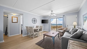 A living room with a balcony, a dining area, and a TV mounted on the wall.