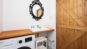 A compact bathroom with a washing machine, a sink, and a wooden door. - Loft Hideaway Studio (Łódź)