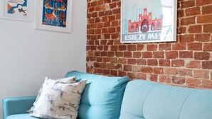 A light blue sofa with a patterned pillow against a brick wall, with two framed posters above. - Loft Hideaway Studio (Łódź)