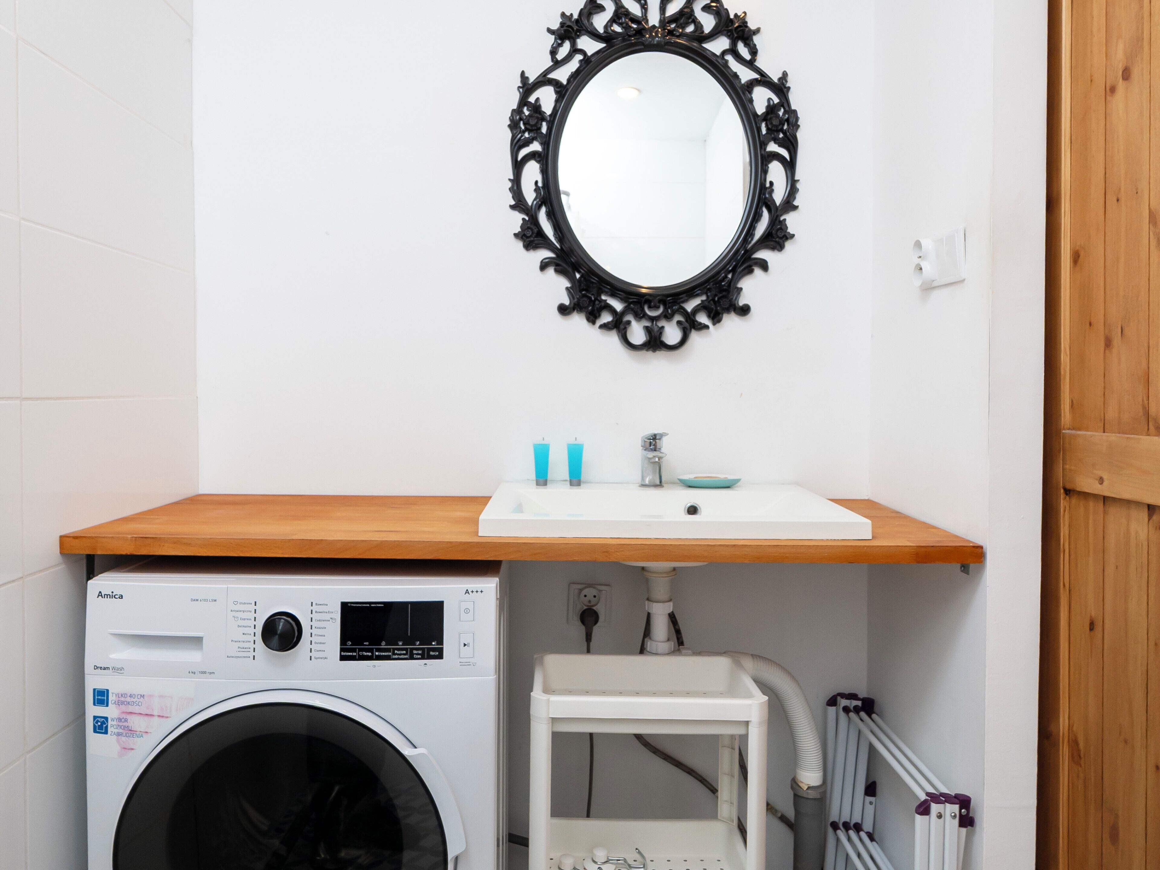 A compact laundry room with a washing machine, a sink, and a mirror.