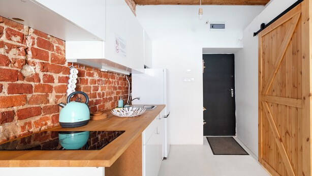 A kitchen with a brick wall, wooden counter, and a black door. - Loft Hideaway Studio (Łódź)