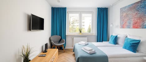 Una habitación de hotel moderna con cama, escritorio, silla, televisor y ventana con cortinas.