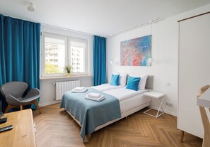 Une chambre moderne avec un lit, un bureau et une chaise. Il y a une fenêtre avec des rideaux, un radiateur et un tableau accroché au mur.