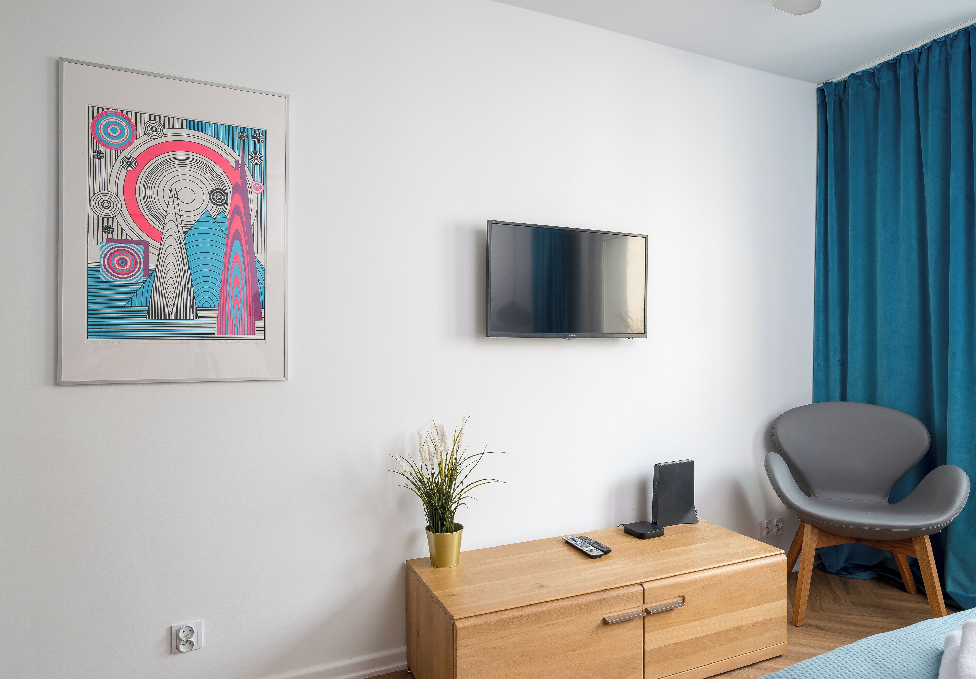 A modern room with a flat-screen TV, a wooden cabinet, a grey chair, and a blue curtain.