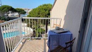 A balcony with a pool view, a table with a chair, and a small table with a book and a ball. - CAP D'AGDE - Port Center // Ref 0142 (CAP D'AGDE)
