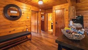 Interior de una cabaña de madera con un banco, un espejo, una cesta de aperitivos y una zona de cocina.