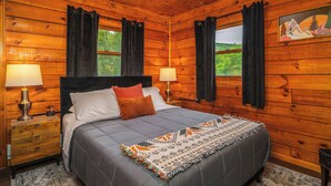 Un dormitorio de cabaña de madera con una cama, dos lámparas de noche, una mesita de noche y una ventana con cortinas.