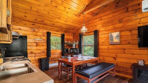 Interior de una cabaña de madera con cocina, comedor y un banco.