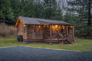 Une cabane en rondins avec un porche, entourée d’arbres.