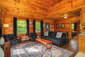 Ein Holzblockhaus-Interieur mit einer Couch, Sesseln, einem Couchtisch und einem Teppich.
