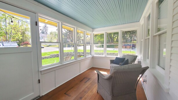 Une véranda avec de grandes fenêtres, des meubles en osier et un plancher en bois.