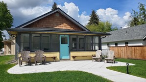Une maison avec un patio couvert, deux chaises, une table et une porte bleue.