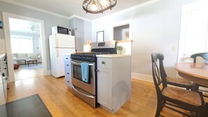 Une cuisine compacte équipée d’un four, d’un micro-ondes et d’un réfrigérateur intégrés. On y trouve une table à manger avec des chaises et une petite plante en pot posée sur le comptoir.