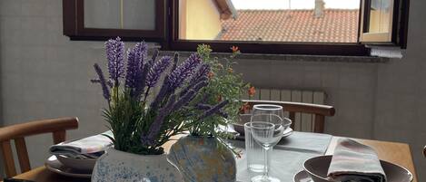 A dining table with a vase of purple flowers, a blue and yellow ceramic pot, and two wine glasses.