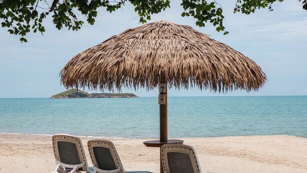 Une plage avec un parasol en chaume et deux chaises longues.