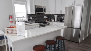 A modern kitchen with white cabinets, a stainless steel refrigerator, a microwave, and a central island with stools.