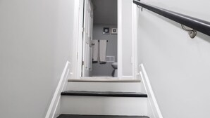 A staircase leading to a bathroom with white walls and a black handrail.