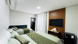 Habitación de hotel con dos camas, un televisor de pantalla plana montado en un panel de madera, una mesita con una toalla y un minibar.