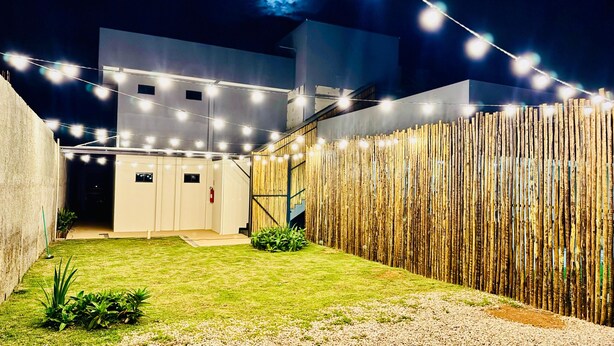 Un espacio exterior moderno con césped, valla de madera y luces colgantes.