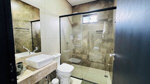 Un baño moderno con ducha de vidrio, lavamanos blanco y retrete.