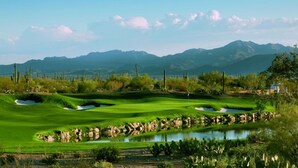 Un campo de golf con búnkeres, un estanque y montañas al fondo.