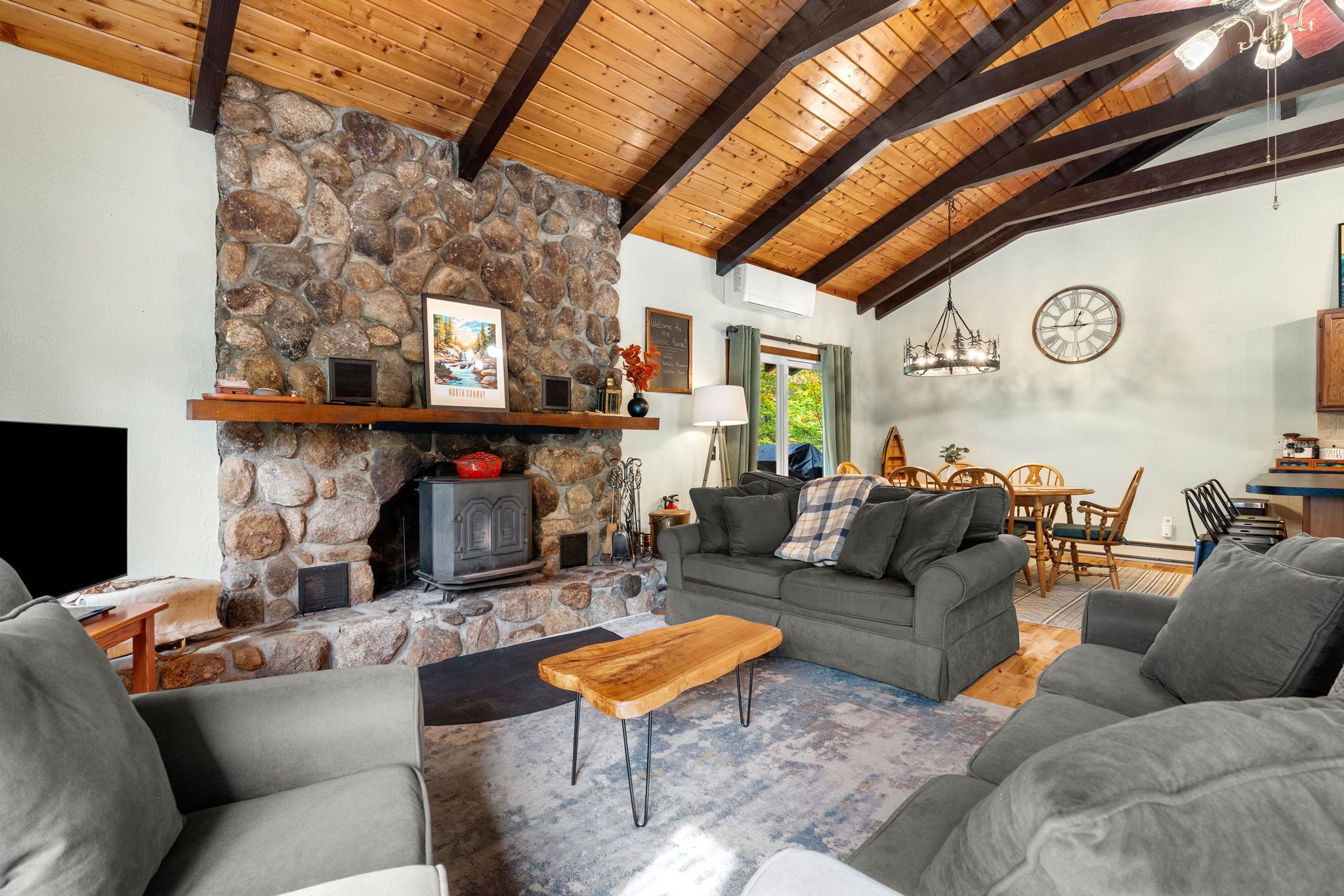 A cozy living room with a stone fireplace, wooden beams, a sofa, and a dining area.