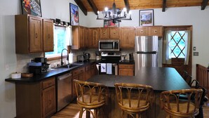 A kitchen with wooden cabinets, a large island with chairs, stainless steel appliances, and a chandelier. - Loose Moose Lodge – Family chalet, fireplace, ski! (Bartlett)