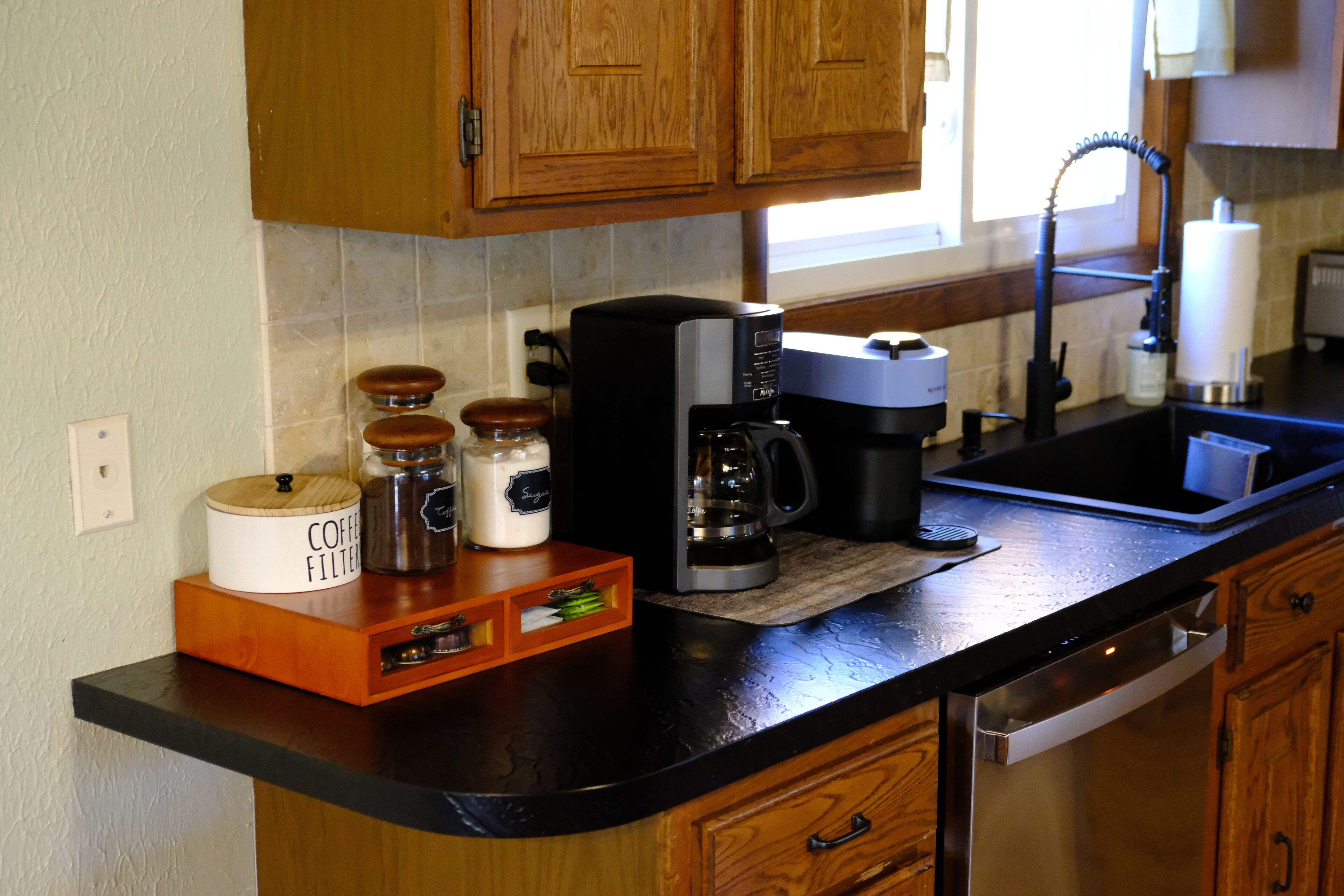 A kitchen with wooden cabinets, a coffee maker, and a coffee grinder on the counter.