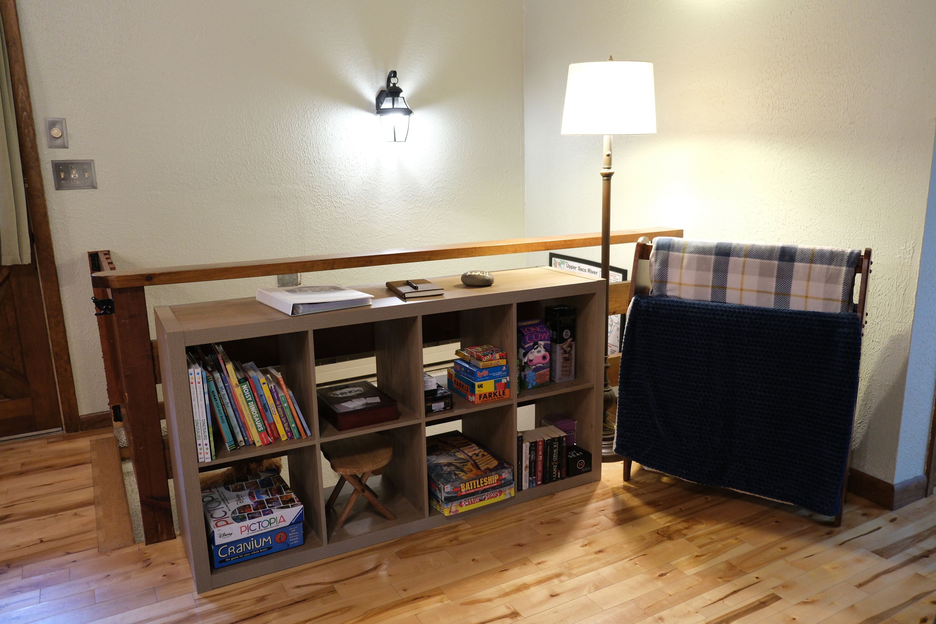 A room with a wooden bookshelf filled with board games, a lamp, and a plaid blanket on a chair.