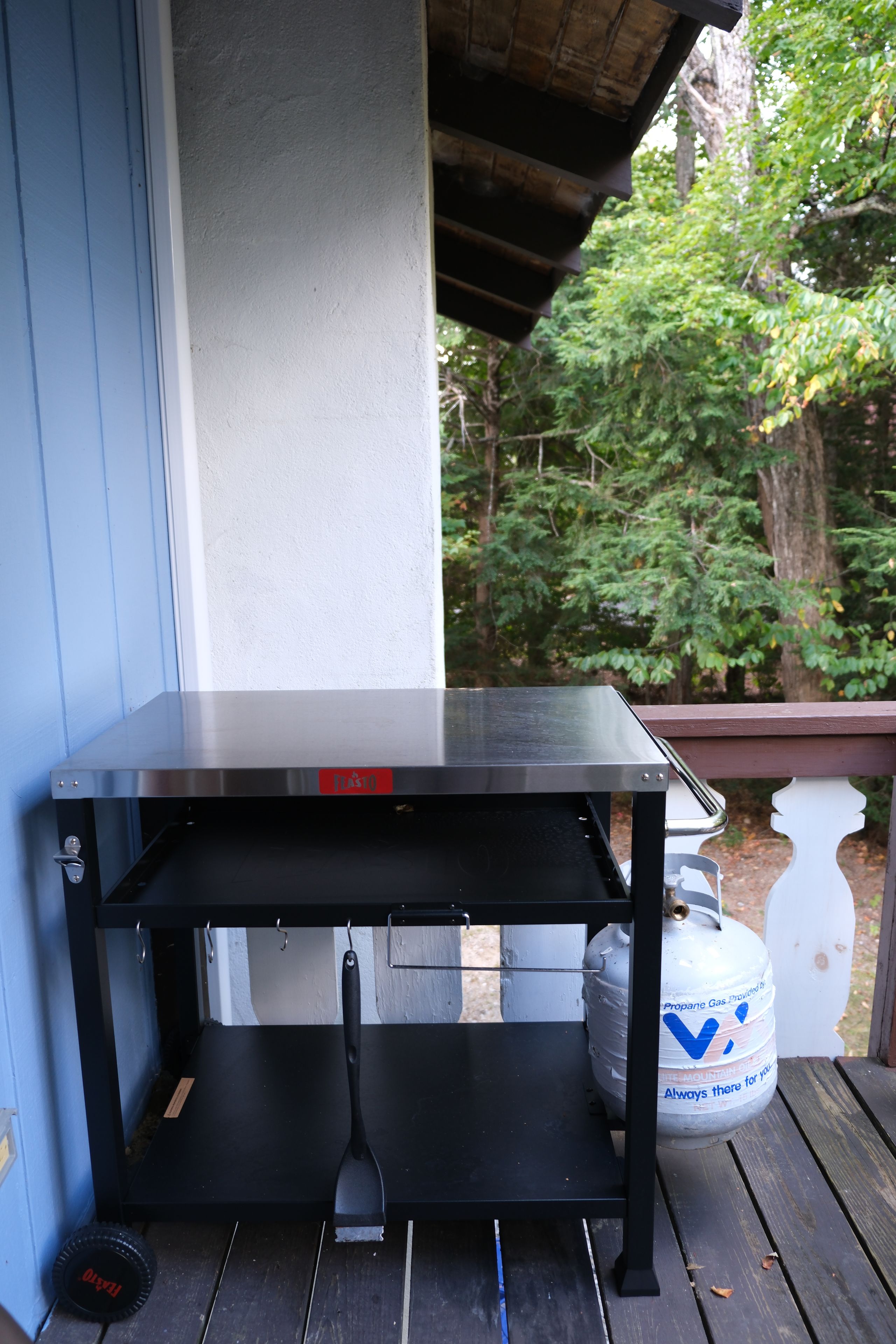 A black metal table with a shelf, a propane gas cylinder, and a black grill on a wooden deck.