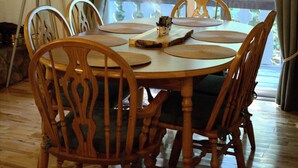 A dining area with a wooden table and chairs, a chandelier, and a view of trees through a window. - Loose Moose Lodge – Family chalet, fireplace, ski! (Bartlett)