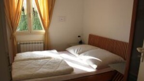 A single bed with a wooden headboard, a nightstand, and a window with curtains. - Bungalow 'Camping Massimo -  2' with Lake View, Private Terrace and Private Garden (Bolsena)