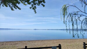 A beach with a wooden fence and a sign, overlooking a calm lake with distant landforms. - Bungalow 'Camping Massimo -  2' with Lake View, Private Terrace and Private Garden (Bolsena)
