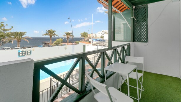 Uma varanda com vista para o mar, uma piscina e palmeiras.