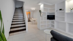 Uma sala de estar moderna com escada, TV de tela plana, prateleiras brancas e um espaço de refeições.