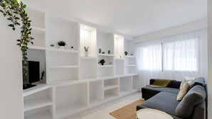 Uma sala de estar moderna com estantes brancas, um sofá cinzento e uma televisão.