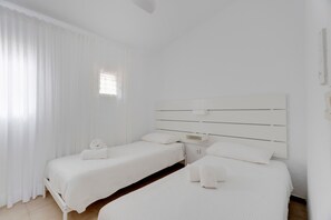 A hotel room with two beds, white bedding, a headboard, and a window with curtains.