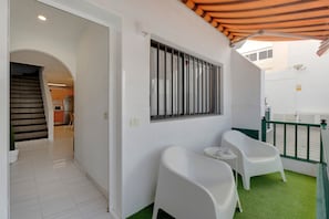 Een modern interieur met een trap naar een keuken, een balkon met een groene balustrade en twee witte stoelen.