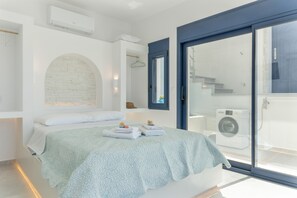 Un dormitorio moderno con cama, lavadora y puerta corrediza de vidrio a un balcón.