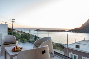 Un balcone con sedie in vimini, un tavolo con frutta e una bottiglia, con vista sulla costa, edifici e un cielo sereno.