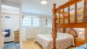 A bedroom with a wooden bed frame, a window with a view, a radiator, and a bedside table with a lamp. - Apartment 'Appartement Entre Mer Et Marais' with Shared Terrace, Wi-Fi and Air Conditioning (Challans)