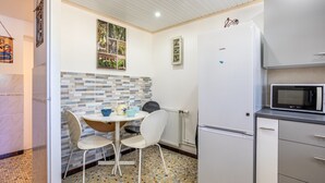 A compact kitchen with a white refrigerator, a microwave, a small table with chairs, and a tiled backsplash. - Apartment 'Appartement Entre Mer Et Marais' with Shared Terrace, Wi-Fi and Air Conditioning (Challans)