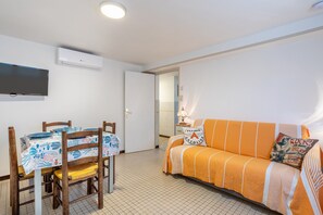 Una habitación con una mesa de comedor, sillas, un sofá, un televisor de pantalla plana y un equipo de aire acondicionado.