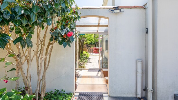 A covered outdoor area with a pathway leading to a glass door, surrounded by greenery and a white wall. - Apartment 'Appartement Entre Mer Et Marais' with Shared Terrace, Wi-Fi and Air Conditioning (Challans)